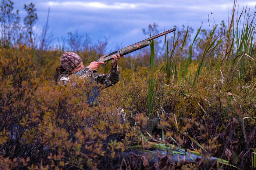 Duck hunter sighting down a bird in a kayak.