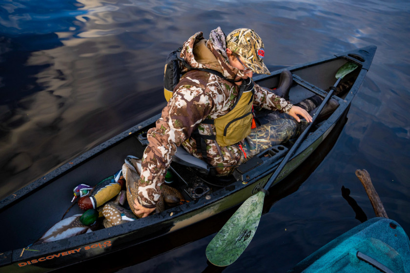 A duck hunter reaching for decoys in their kayak.