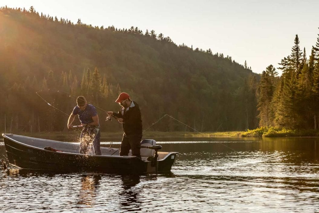 Two anglers fish in a lake from a fishing boat.