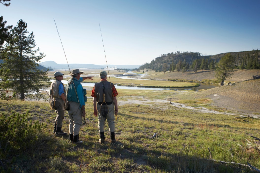 Three men in fishing vests looking at river, rear view