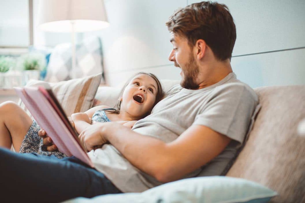 A father and daughter sitting on the couch reading a book