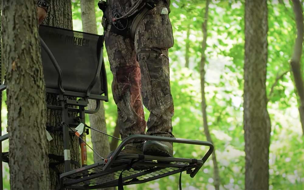 Hunter stands on a hang-on treestand in the woods