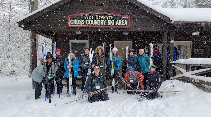 a group picture in falling snow outside a cross-country ski lodge