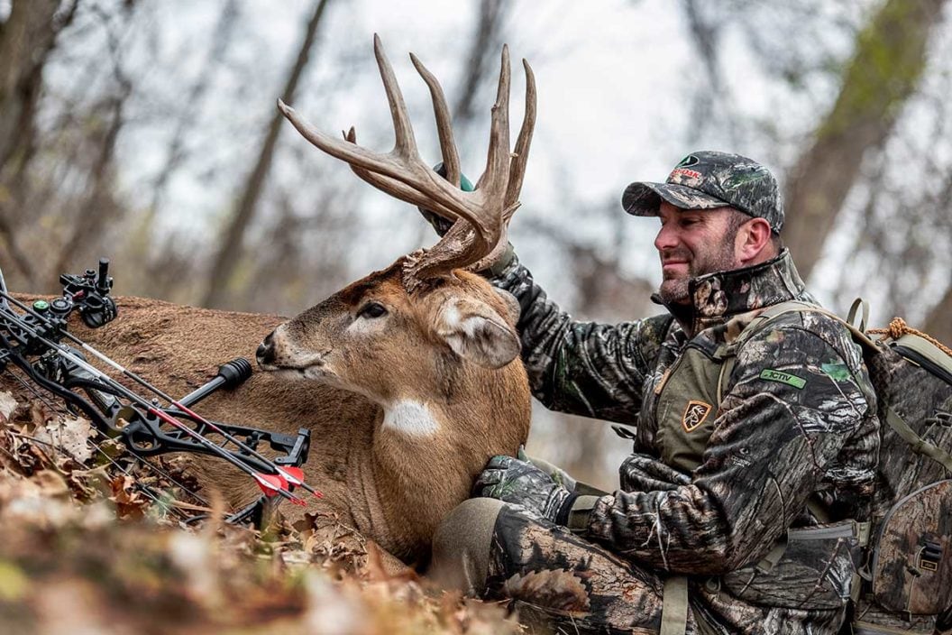 Deer hunter neels over a buck he just hunted