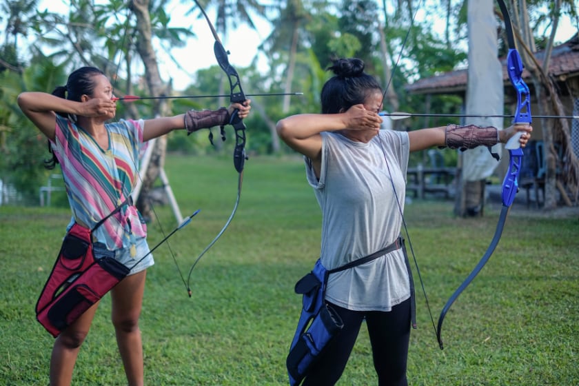 Close-up shot of two female friends practicing archery in the outdoor shooting range.
