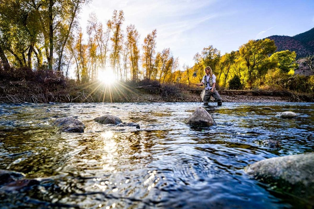 A female fly angler stands in a river and casts a line