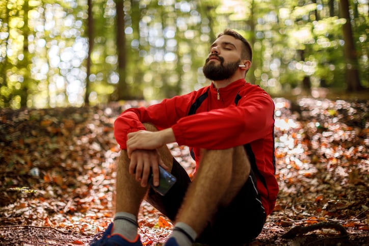 Portrait of relaxed young man with bluetooth headphones in forest