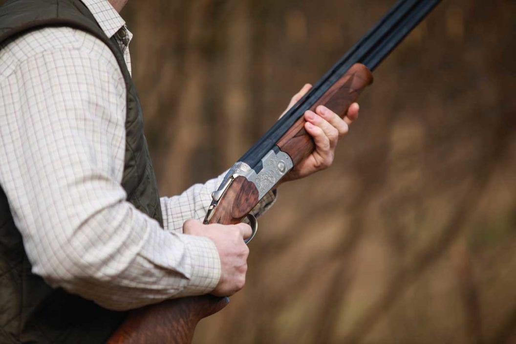 Man holds a shotgun while practicing wingshooting with clay targets