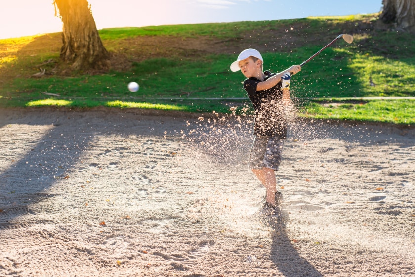 boy golfing in sand