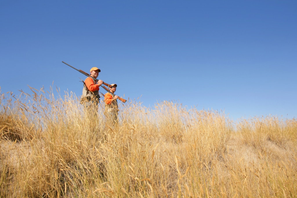 two men wearing orange standing in field