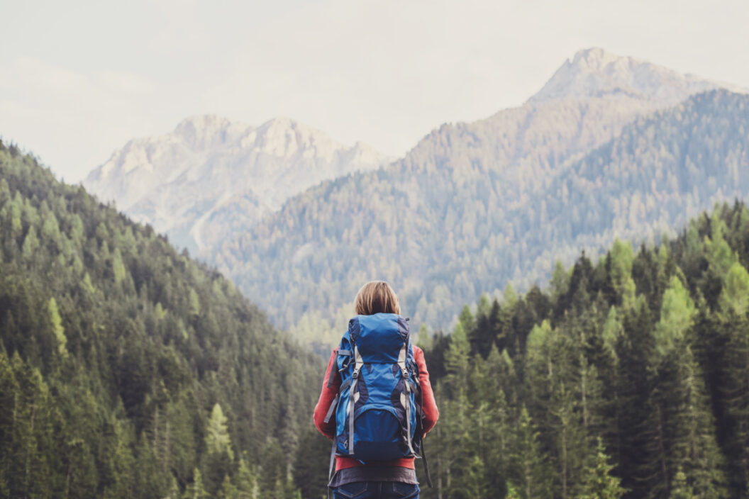 Woman hiking with background of mountains and trees, with a backpack on